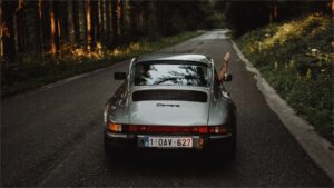森の道を走るクラシックカーと手を出すドライバー